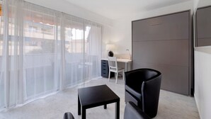 A modern room with a large window, a desk, a chair, a small table, and a wardrobe. - Apartment 'Couronne Du Cros' with Sea View, Wi-Fi and Air Conditioning (Cagnes-sur-Mer)