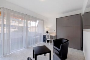 A modern room with a large window, a desk, a chair, a small table, and a wardrobe.
