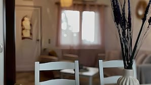 Zona pranzo con tavolo apparecchiato per quattro persone, un vaso con canne decorative e vista su un soggiorno con divano e finestra.