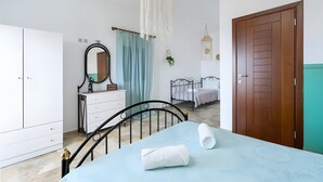 Una camera da letto con un letto, un armadio, una cassettiera, uno specchio, una lampada a sospensione e una porta.