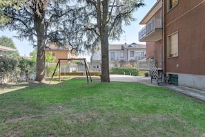 A residential area with a grassy yard, a swing set, and a building with a balcony. - 'Casa Cedrus' with Shared Garden (Lainate)