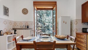Un'area pranzo con un tavolo apparecchiato per quattro persone, sedie, un frigorifero, un forno a microonde e vista sugli alberi attraverso una finestra.