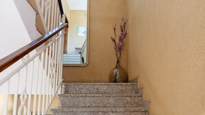 Una scala con ringhiera in legno, un vaso con fiori viola e uno specchio che riflette una stanza con un letto e una finestra.