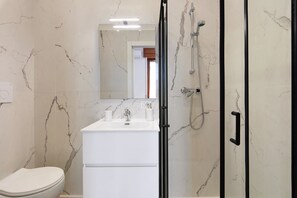 Un bagno con il water, un lavandino, uno specchio e un box doccia.