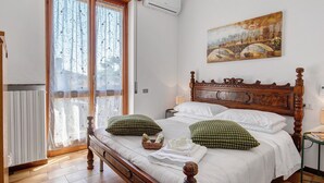 Un letto rifatto con cuscini, una testiera in legno, un quadro al muro e una finestra con tende.