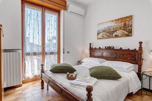 Un letto rifatto con cuscini, una testiera in legno, un quadro al muro e una finestra con tende.