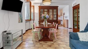 Zona pranzo con tavolo in legno, sedie, televisore a parete e mobile con ante in vetro.