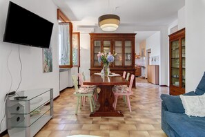 Zona pranzo con tavolo in legno, sedie, televisore a parete e mobile con ante in vetro.