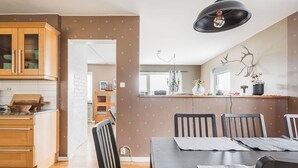 Ett modernt kök med träskåp, en matplats med ett mörkt träbord och stolar samt en hänglampa ovanför bordet.