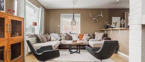A modern living room with a sectional sofa, two black chairs, a wooden cabinet, and a hanging light fixture.