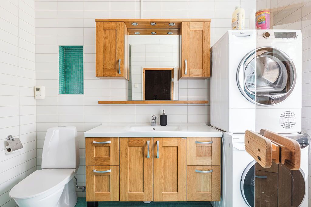A compact bathroom with a toilet, sink, wooden cabinets, a mirror, and a washing machine.