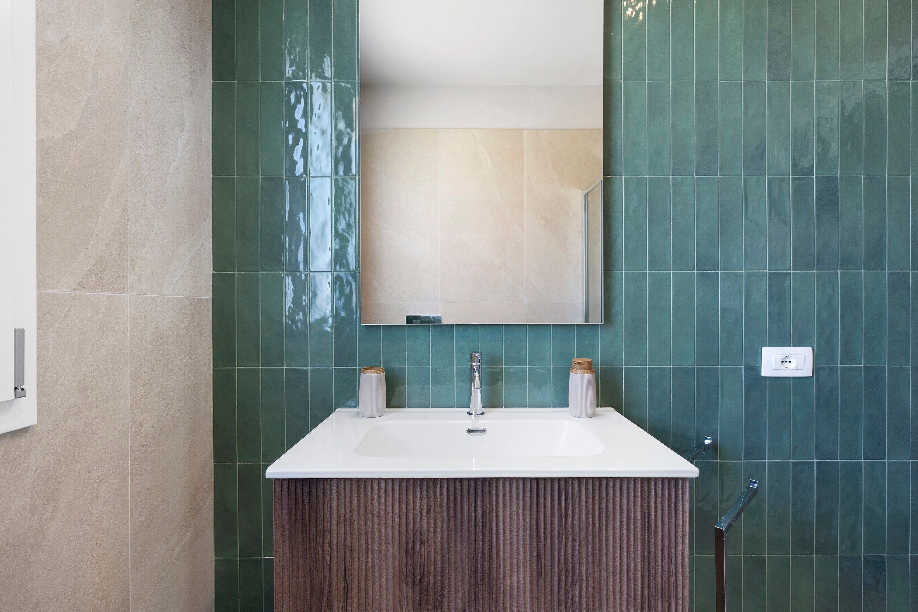 Ein Badezimmer mit einem weißen Waschbecken, einem Spiegel und grünen Fliesen.