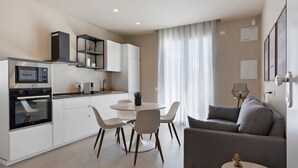 Une cuisine moderne avec des meubles blancs, une table à manger avec des chaises, un four encastré et un réfrigérateur.