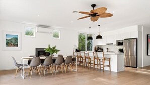 Une cuisine moderne avec des meubles blancs, un réfrigérateur en acier inoxydable et un coin repas comprenant une table et des chaises en bois.