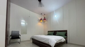 A bedroom with a bed, a chair, a mirror, and pendant lights. - Slate Majestic 1BHKs Sector 53 Noida (Noida)