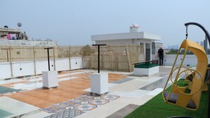 A rooftop terrace with patterned flooring, a swing chair, and a small building with a water tank. - Slate Majestic 1BHKs Sector 53 Noida (Noida)