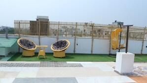A rooftop terrace with two wicker chairs, a small table, and a decorative metal sculpture. - Slate Majestic 1BHKs Sector 53 Noida (Noida)