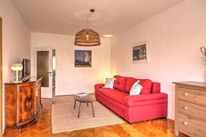 Ein Wohnzimmer mit einem roten Sofa, einem Holzkasten und einer Pendelleuchte.