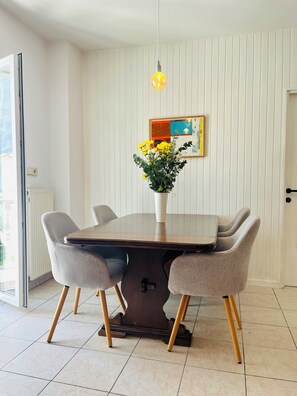 Ein Essbereich mit einem Holztisch, vier grau gepolsterten Stühlen, einer Vase mit gelben Blumen, einer Pendelleuchte und einem gerahmten Bild an der Wand.