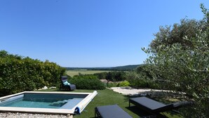 En swimmingpool med udsigt over landskabet, omgivet af grøn vegetation og en klar himmel.