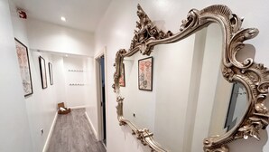Ein Korridor mit einem großen, verzierten Spiegel, gerahmten Kunstwerken an den Wänden und einem Holzboden.