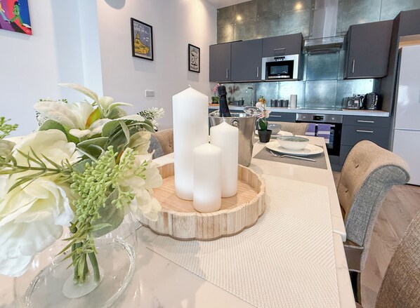 A modern kitchen with stainless steel appliances, a dining area with a white table and a vase of flowers. - Yellow Submarine Apartments - Sleeps 19 (Liverpool)