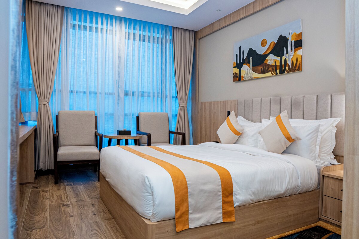 A hotel room with a large bed, two armchairs, a small table, and a painting on the wall.
