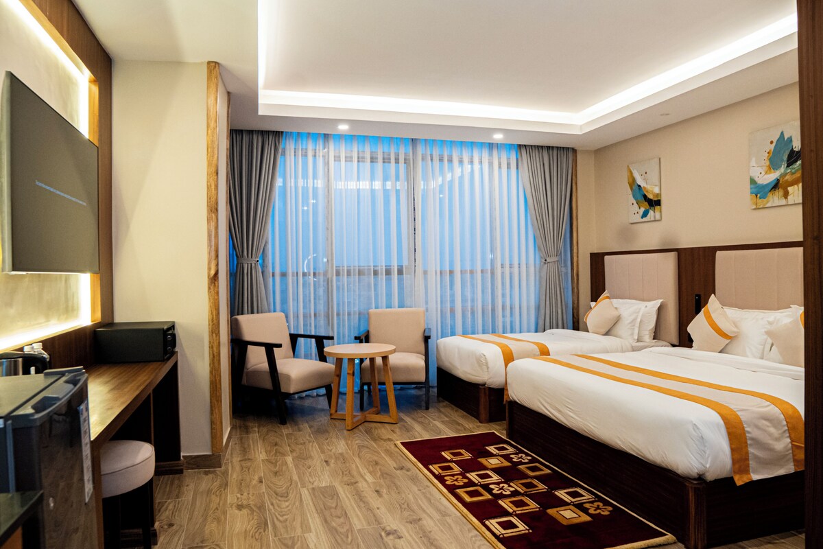 A hotel room with a bed, a desk, a chair, a small table, and a TV.