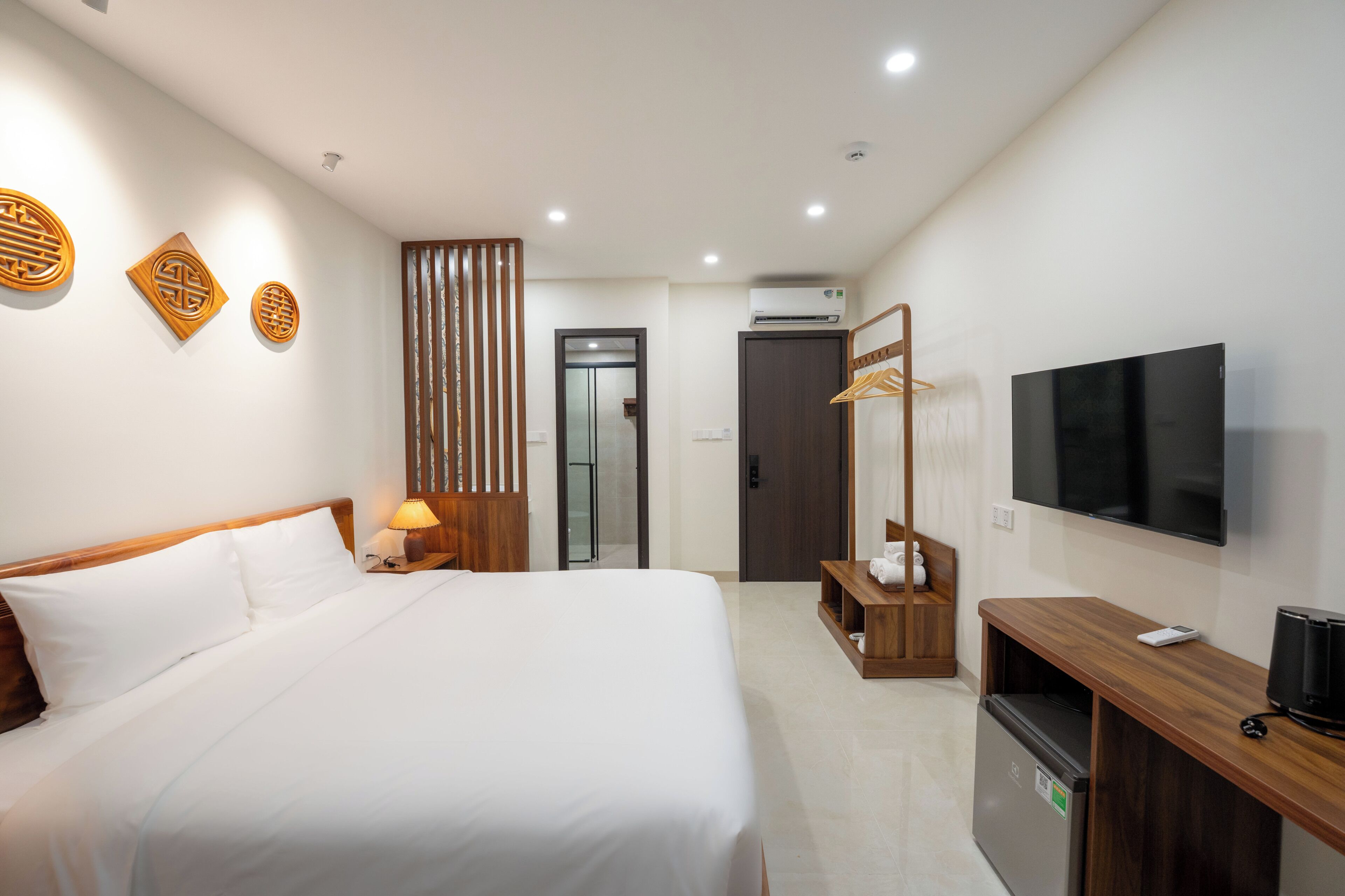 A hotel room with a bed, bedside table, lamp, TV, and a wardrobe.