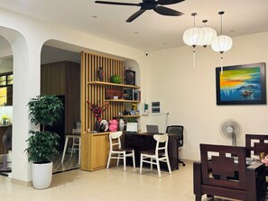 Una sala de estar moderna con un separador de madera, un comedor con mesa y sillas, un ventilador de techo y un cuadro en la pared.