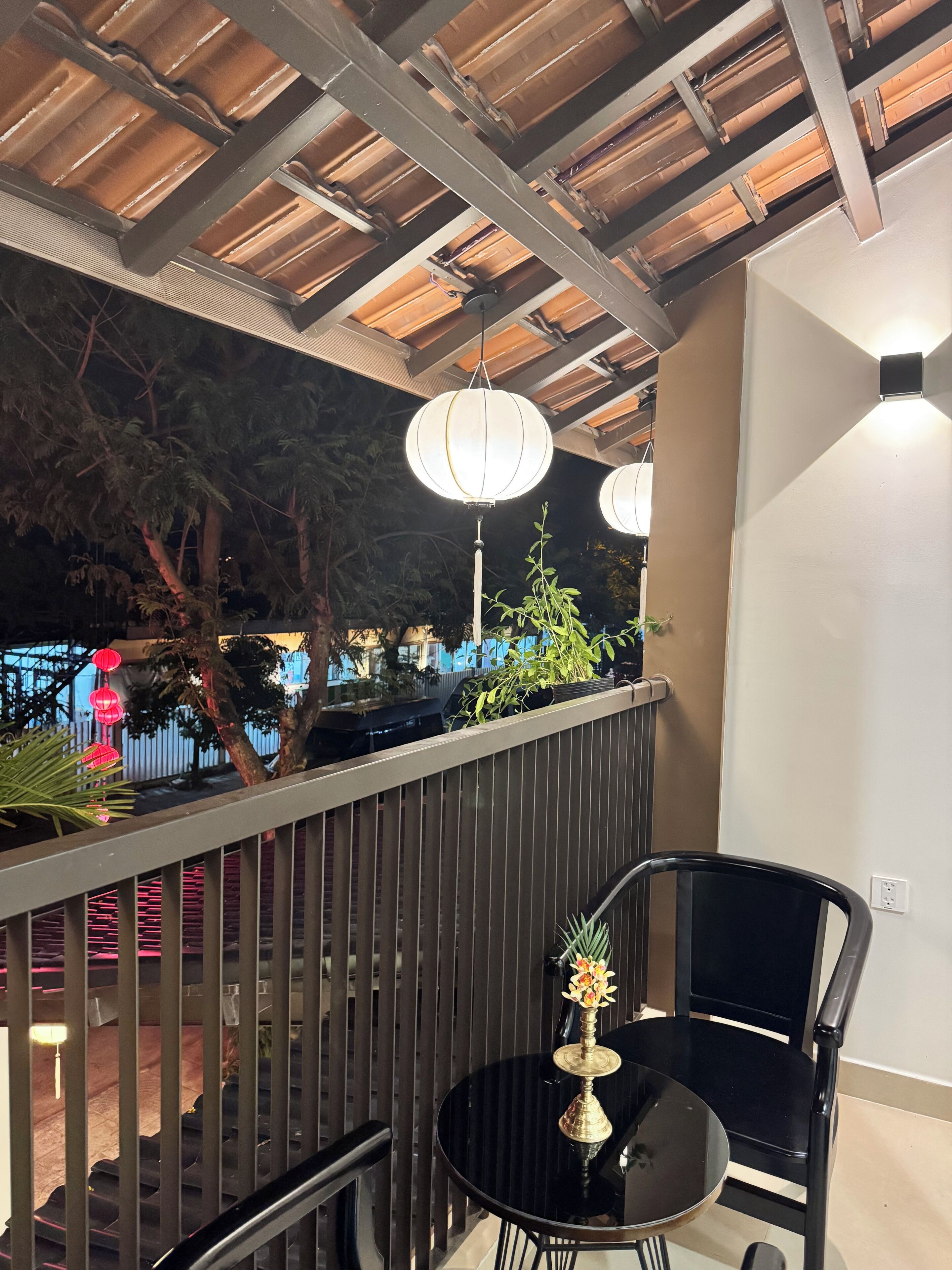 A balcony with a metal railing, a round black table with a vase, and hanging lanterns.