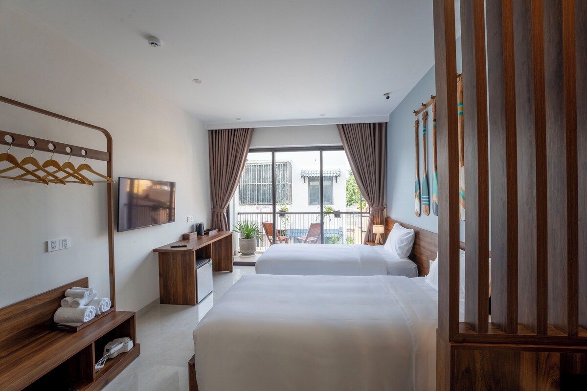 A hotel room with two beds, a TV, a desk, and a balcony with a view.