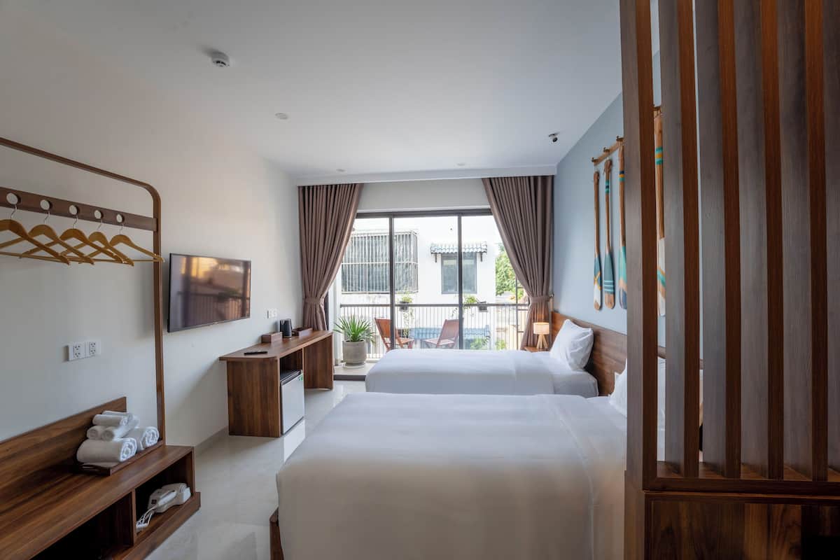 A hotel room with two beds, a TV, a desk, and a balcony with a view.