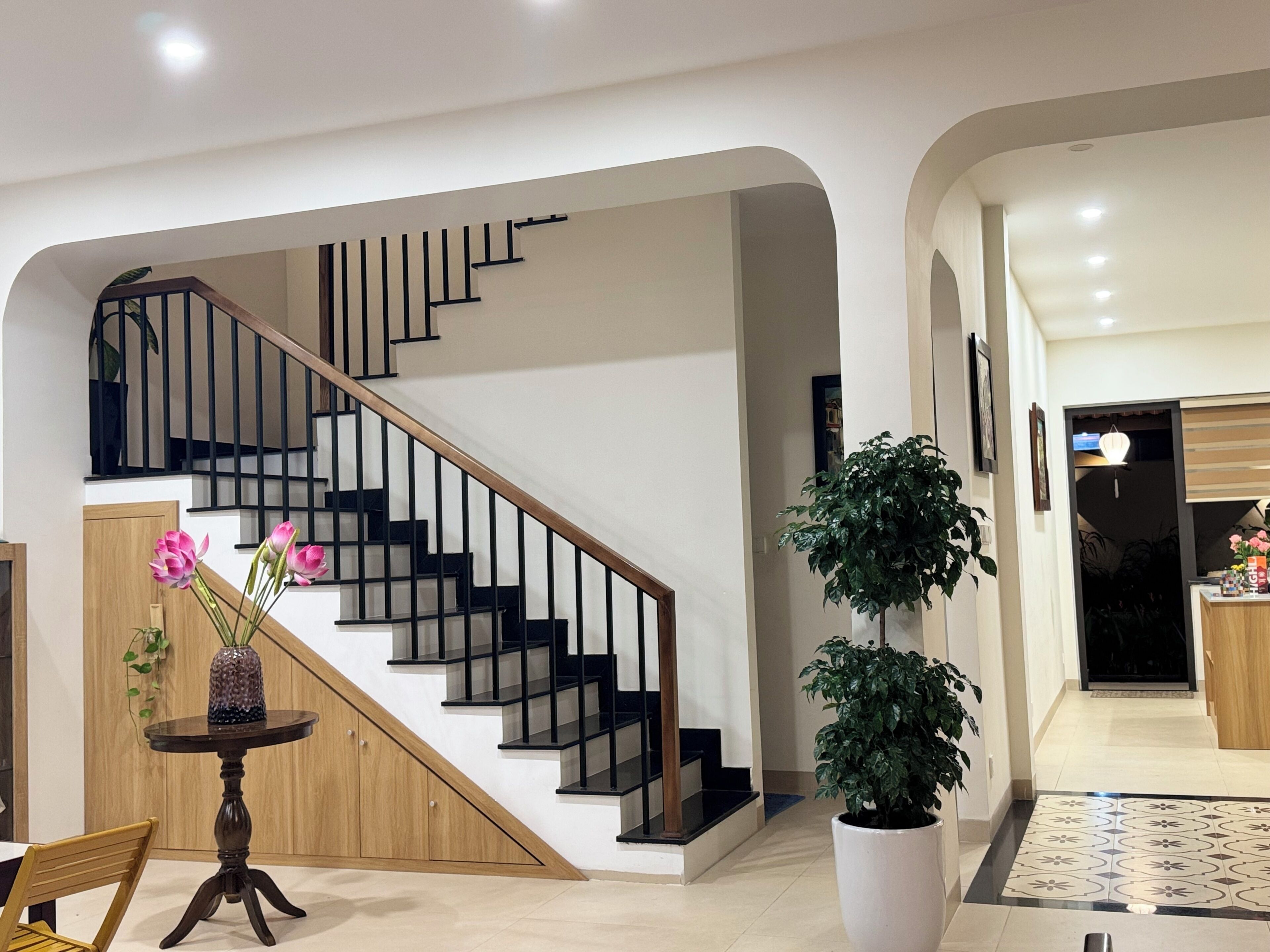 A modern interior with a staircase, a dining area, and a large potted plant.