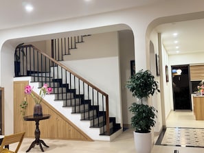 Un interior moderno con una escalera, una zona de comedor y una planta grande en maceta.