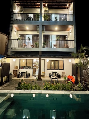 Un edificio de varios pisos con balcones, piscina y mobiliario de exterior.