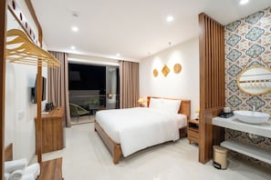 A modern hotel room with a bed, wooden furniture, a bathroom with a sink and mirror, and a view of the outdoors.
