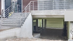 Een trap die leidt naar een overdekt gebied, met een metalen hekwerk en betonnen treden, en een gedeeltelijk zichtbare deur.