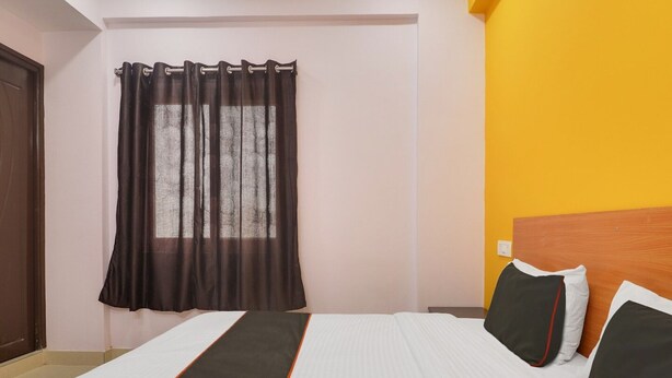 Een hotelkamer met een bed, een raam met gordijnen, een houten hoofdeinde en een gele wand.