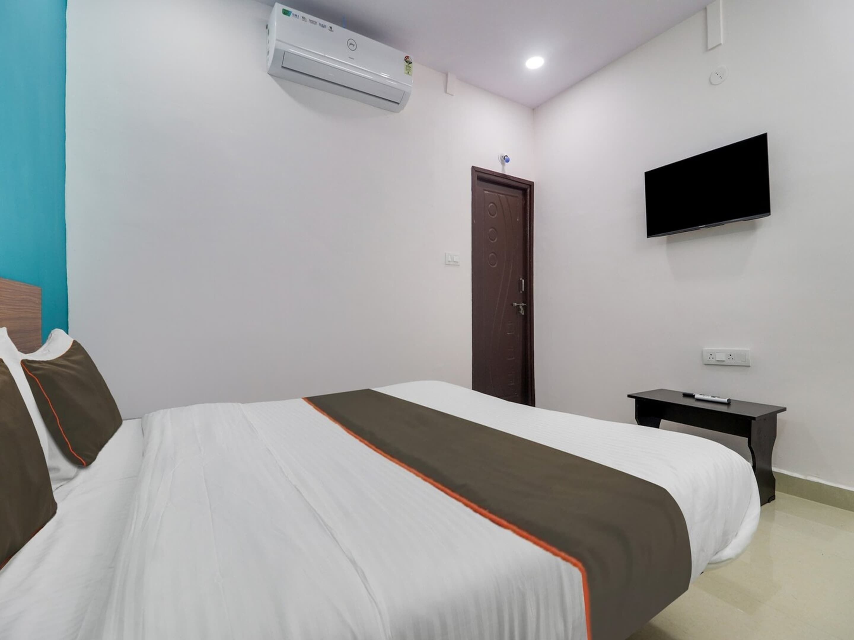 A hotel room with a bed, a TV mounted on the wall, a door, and an air conditioning unit.