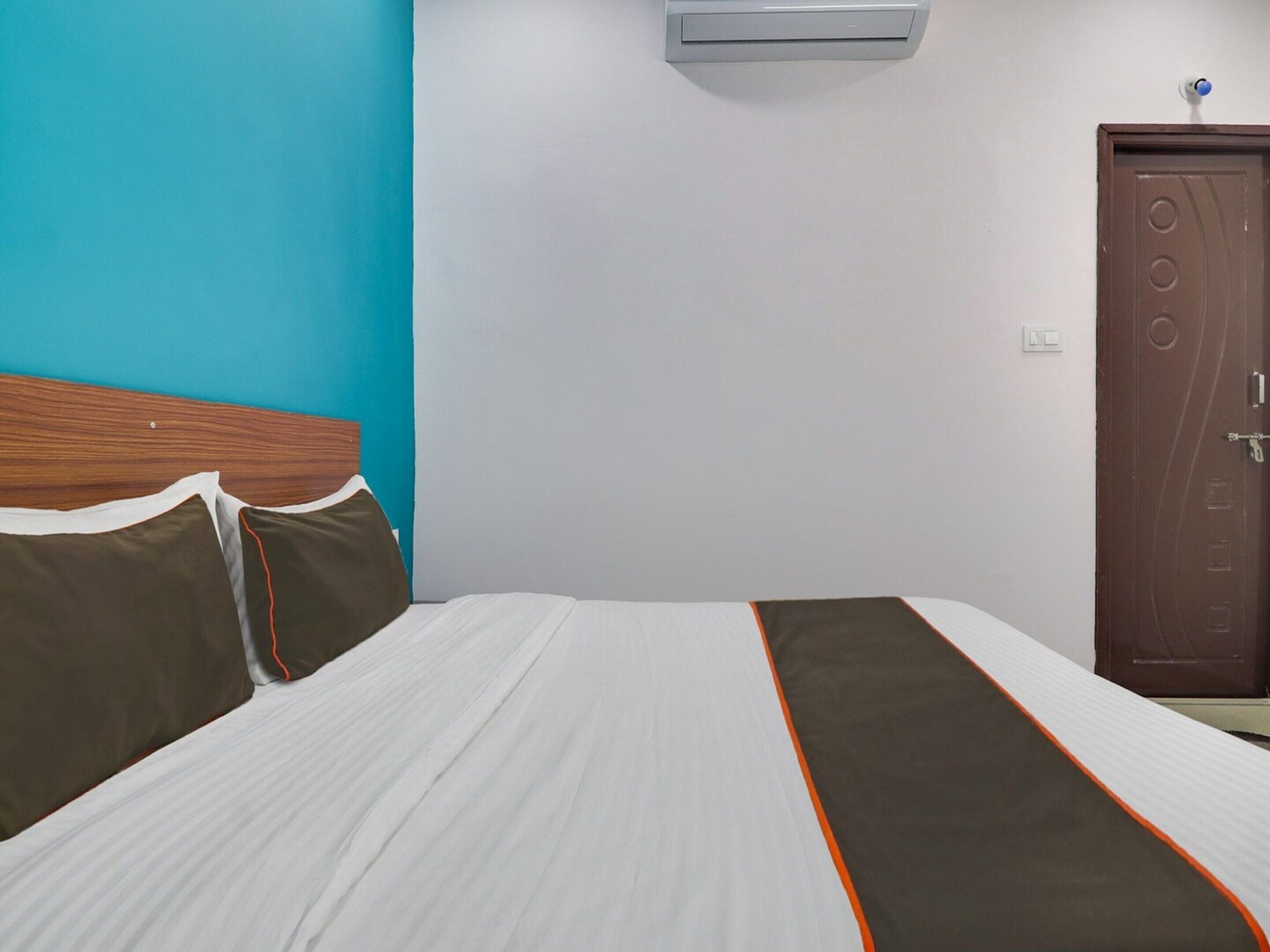 A hotel room with a bed, a wooden headboard, a door, and an air conditioning unit.