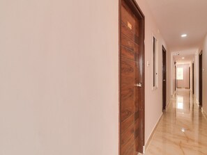 A hallway with wooden doors, a marble floor, and a light-colored wall. - Super Collection O Rbs Kothapet-nagole Road (Hyderabad)