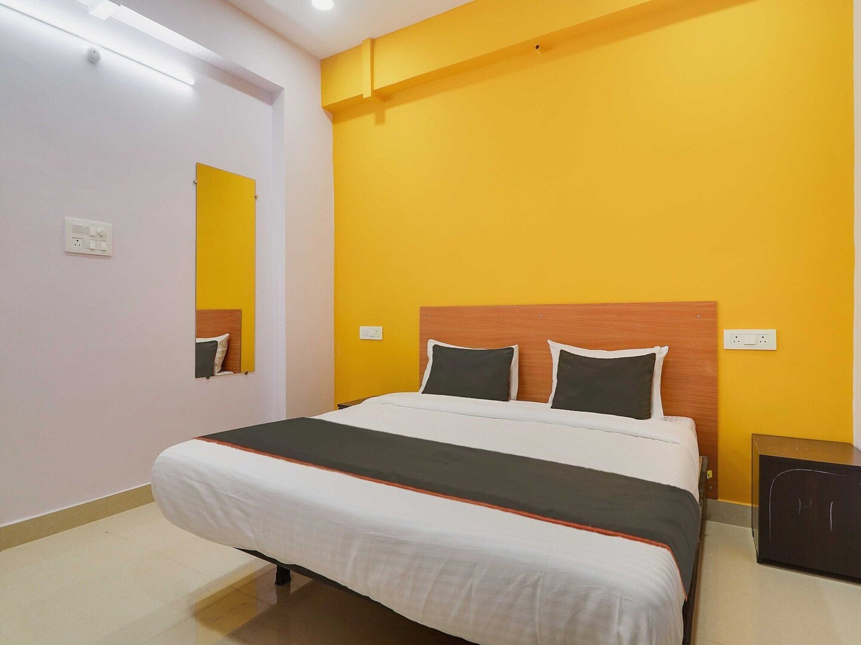 A hotel room with a bed, a nightstand, a mirror, and a wall socket.