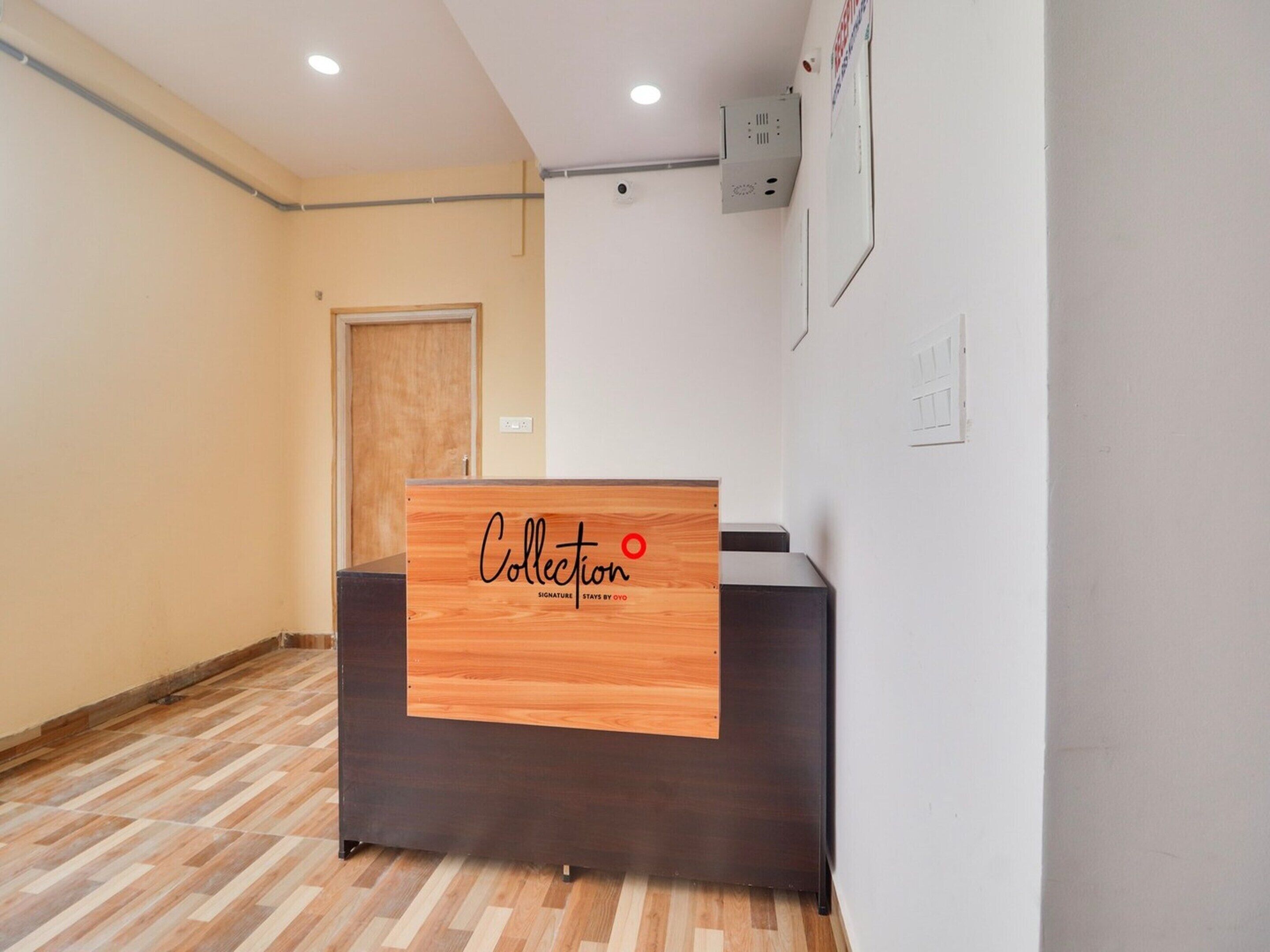 Un mostrador de recepción con encimera de madera y base negra, una puerta de madera y una pared blanca con una lámpara fijada.