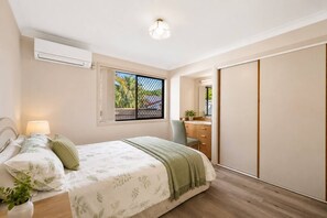 Ein Schlafzimmer mit Bett, Nachttisch, Lampe, Fenster mit Aussicht und einem Schiebetürenschrank.