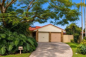 Ein Wohnhaus mit Garage, umgeben von üppigem Grün und blauem Himmel.