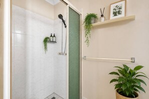 Ein Badezimmer mit Dusche, Handtuchhalter, einer Topfpflanze und einem Ablagefach für Toilettenartikel.