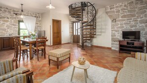 A living room with a stone wall, a spiral staircase, a dining area with wooden furniture, and a television on a stone wall. - Holiday house with pool for 10 persons, 2 separate accommodation units,in Porec (Dračevac)