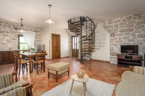 Ein Wohnzimmer mit Steinsandsteinwand, einer Wendeltreppe, einem Essbereich mit Holzmöbeln und einem Fernseher an einer Steinsandsteinwand.