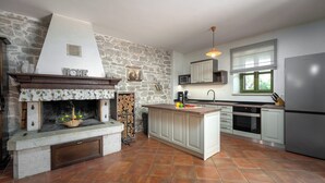 A kitchen with a stone wall, a fireplace, a central island, and modern appliances. - Holiday house with pool for 10 persons, 2 separate accommodation units,in Porec (Dračevac)